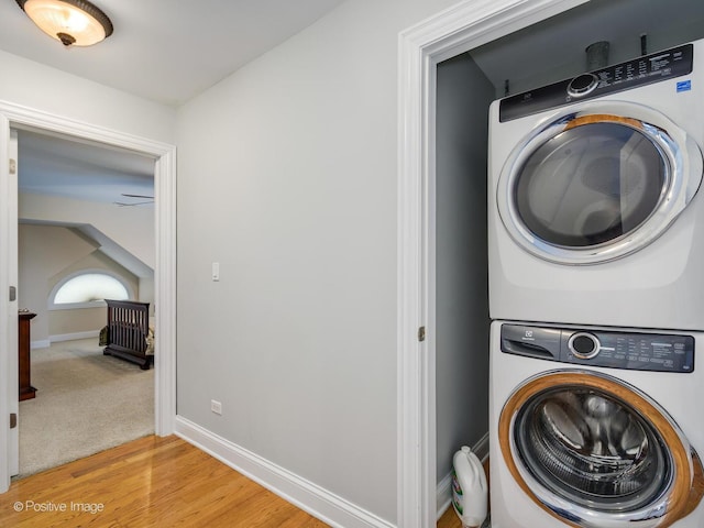 laundry area with baseboards, light wood-style floors, laundry area, and stacked washer / dryer