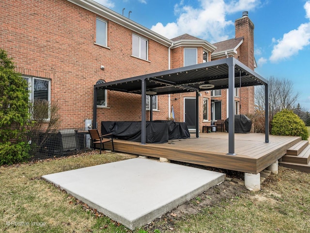 rear view of property featuring a patio, a chimney, brick siding, and a wooden deck