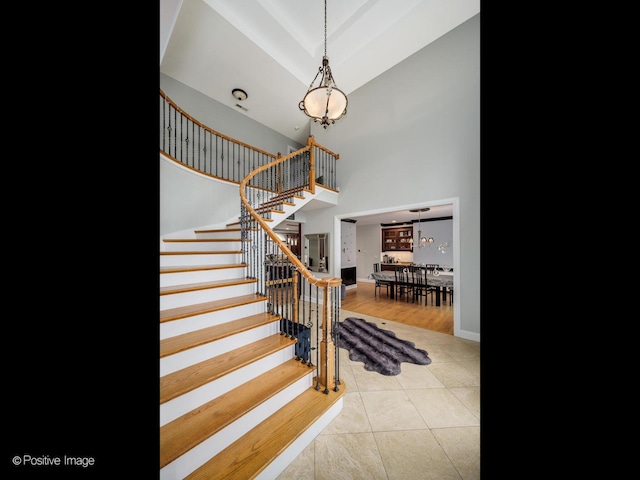 staircase with an inviting chandelier, a high ceiling, baseboards, and tile patterned floors