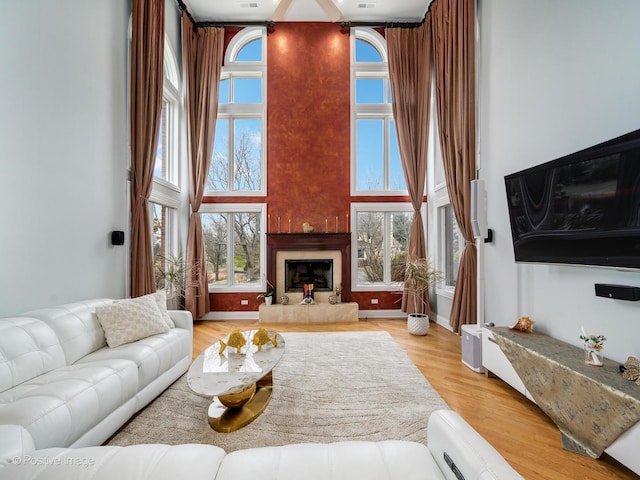 living area with a healthy amount of sunlight, a glass covered fireplace, a high ceiling, and wood finished floors