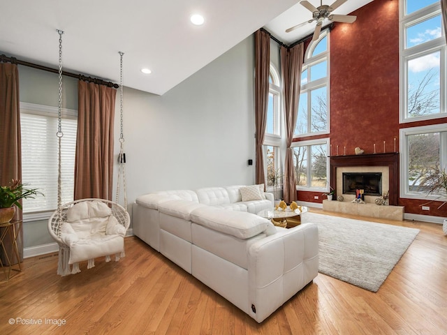 living room featuring recessed lighting, a fireplace with raised hearth, baseboards, ceiling fan, and light wood-type flooring
