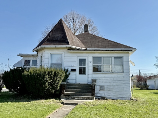 victorian house with a front lawn, a shingled roof, a chimney, and entry steps