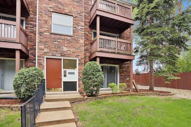exterior space with brick siding, fence, a lawn, and a balcony
