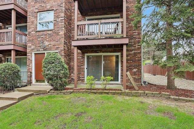 exterior space featuring a balcony, brick siding, fence, and a lawn