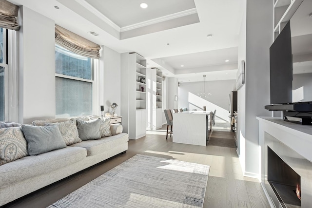 living area with a tray ceiling, recessed lighting, visible vents, and wood finished floors