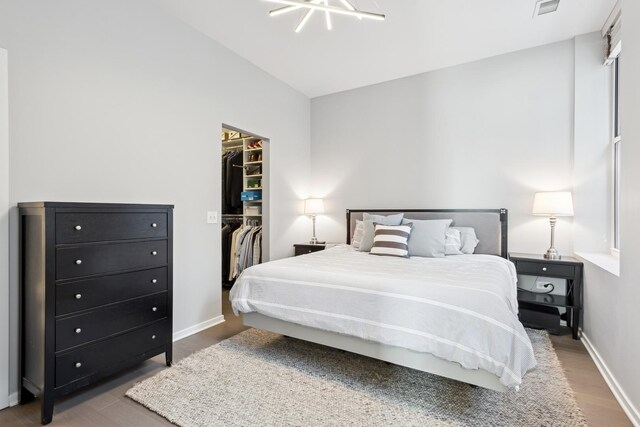 bedroom featuring a walk in closet, a closet, baseboards, visible vents, and wood finished floors