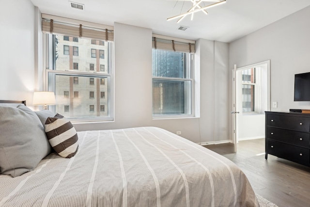 bedroom featuring an inviting chandelier, visible vents, wood finished floors, and baseboards