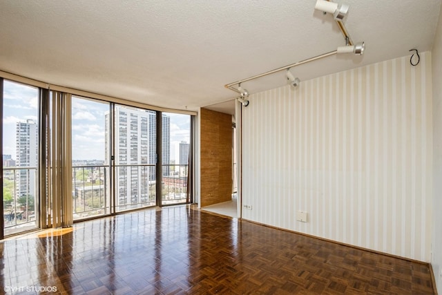 empty room featuring a view of city, wallpapered walls, a textured ceiling, floor to ceiling windows, and baseboards