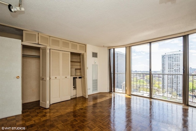 unfurnished bedroom with floor to ceiling windows, a textured ceiling, multiple windows, access to exterior, and a city view