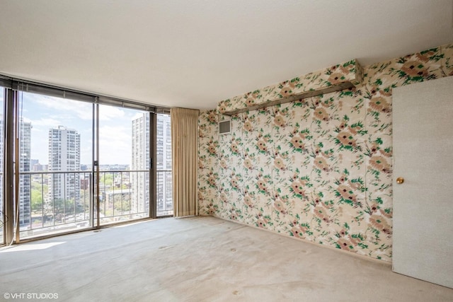 empty room with a city view, wallpapered walls, carpet, and a wall of windows