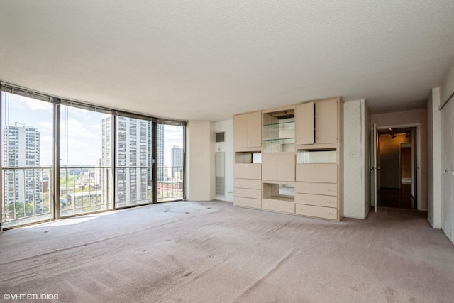 unfurnished living room with light carpet, a city view, a textured ceiling, and floor to ceiling windows