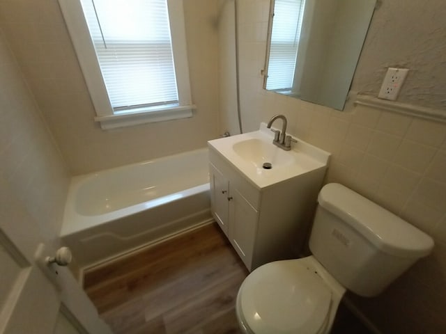 bathroom with toilet, wood finished floors, a bathing tub, tile walls, and vanity
