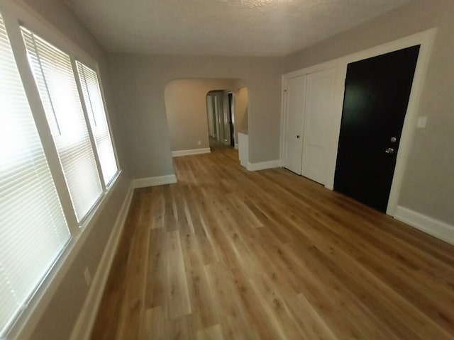 unfurnished room featuring arched walkways, baseboards, and light wood-style flooring
