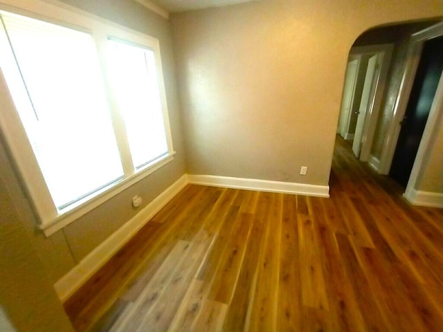spare room with baseboards, arched walkways, and wood finished floors