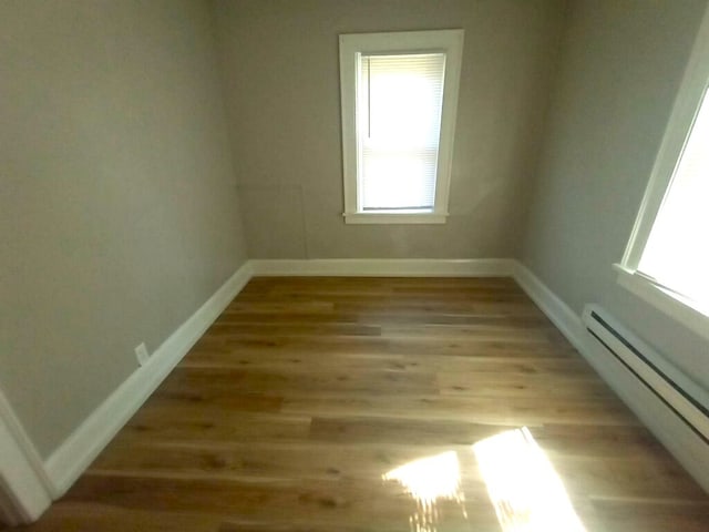 unfurnished room with a baseboard heating unit, baseboards, and wood finished floors
