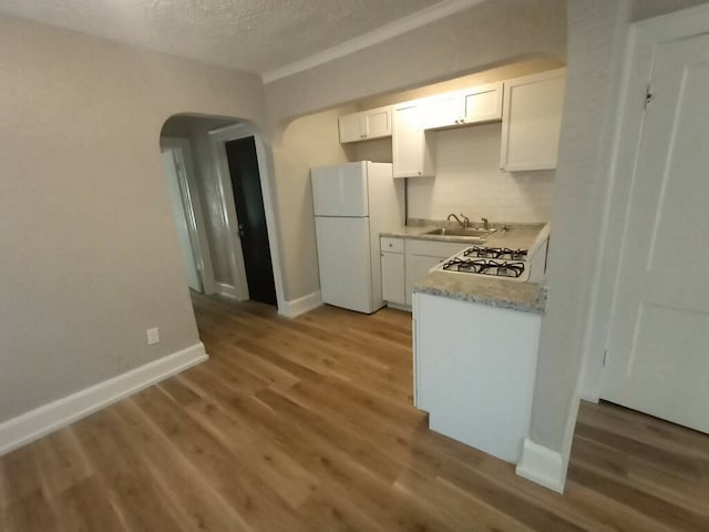 kitchen featuring freestanding refrigerator, light wood finished floors, a sink, and arched walkways