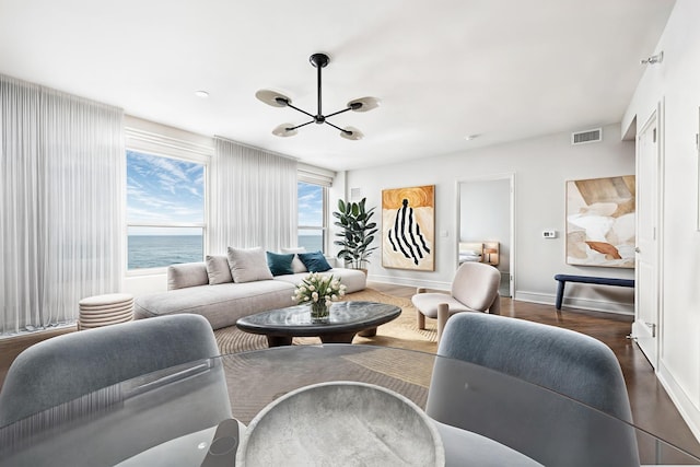 living room featuring a water view, visible vents, baseboards, a chandelier, and dark wood-style floors