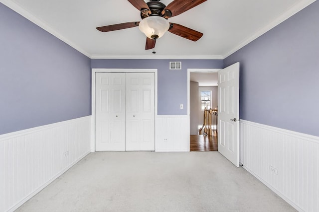 unfurnished bedroom featuring carpet, crown molding, visible vents, and a wainscoted wall