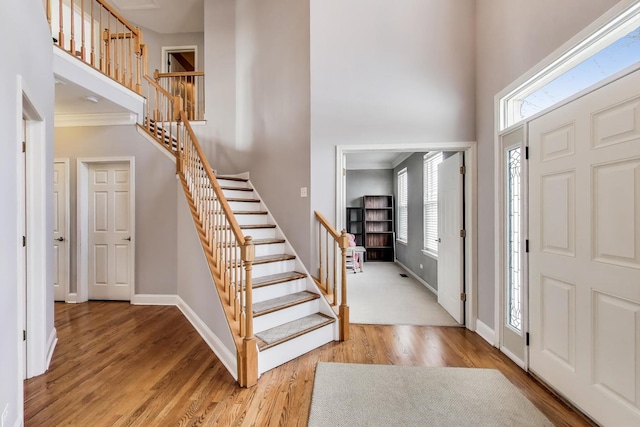 foyer entrance with stairway, a high ceiling, baseboards, and wood finished floors
