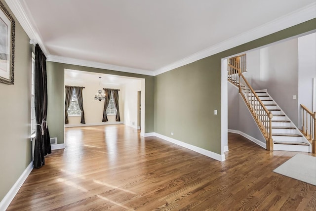 unfurnished living room with an inviting chandelier, stairway, wood finished floors, and crown molding