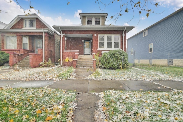 bungalow-style home featuring brick siding, covered porch, and fence