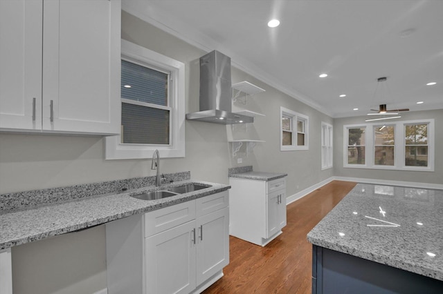 kitchen featuring a sink, wall chimney range hood, wood finished floors, light stone counters, and white cabinets