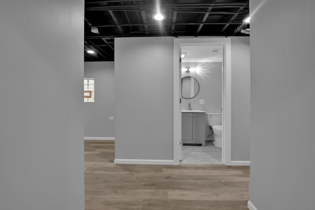 corridor featuring wood finished floors, baseboards, and a sink