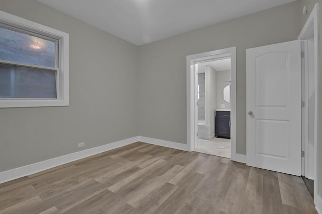unfurnished bedroom with connected bathroom, wood finished floors, and baseboards