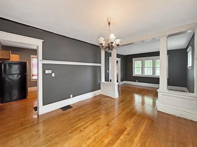 unfurnished dining area with visible vents, a chandelier, decorative columns, and light wood-style flooring