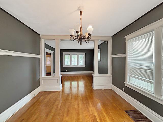 unfurnished dining area featuring an inviting chandelier, baseboards, light wood-type flooring, and visible vents