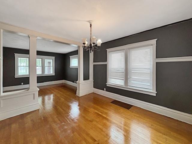 unfurnished dining area with baseboards, a chandelier, wood finished floors, and visible vents
