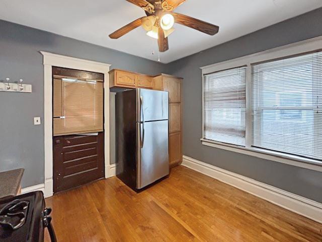 kitchen with wood finished floors, a ceiling fan, light brown cabinetry, freestanding refrigerator, and baseboards