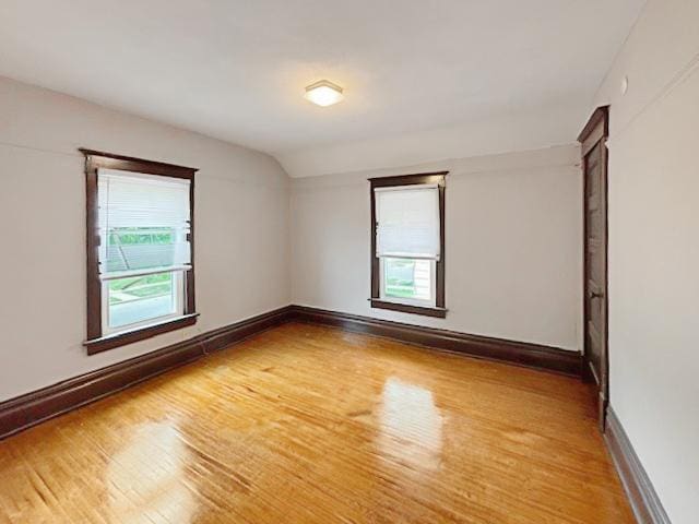 unfurnished room with vaulted ceiling, light wood-style flooring, and baseboards
