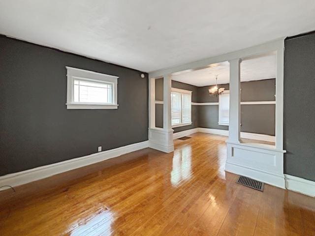 empty room with a chandelier, visible vents, wood finished floors, and baseboards