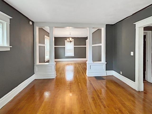 empty room featuring baseboards, built in features, a chandelier, wood finished floors, and ornate columns