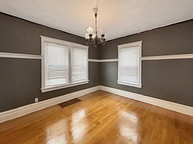 spare room with baseboards, an inviting chandelier, visible vents, and wood finished floors