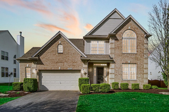 traditional home featuring driveway, brick siding, a yard, a garage, and a shingled roof