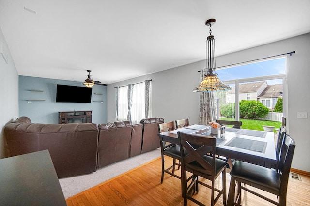 dining space featuring ceiling fan, light wood-style floors, and a glass covered fireplace
