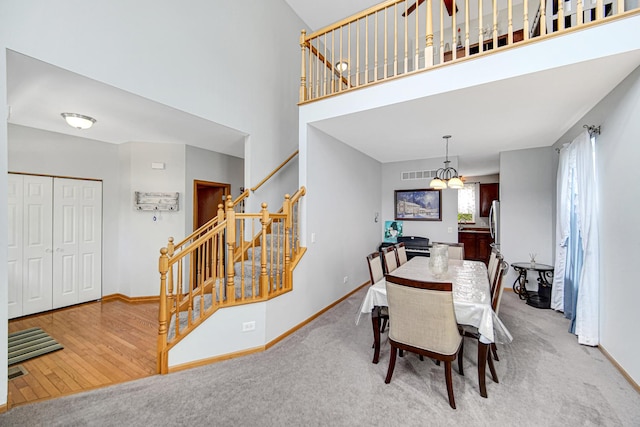 dining space featuring stairs, baseboards, wood finished floors, a towering ceiling, and a chandelier