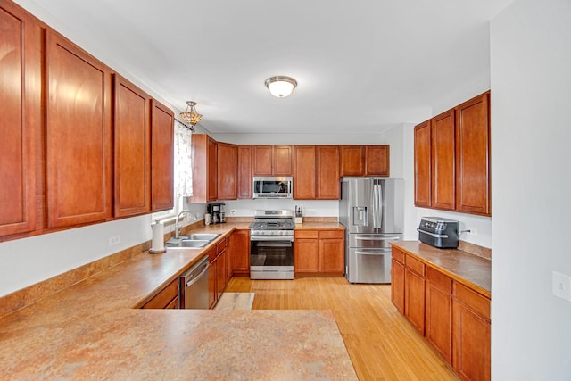 kitchen with stainless steel appliances, a sink, brown cabinets, and light wood-type flooring