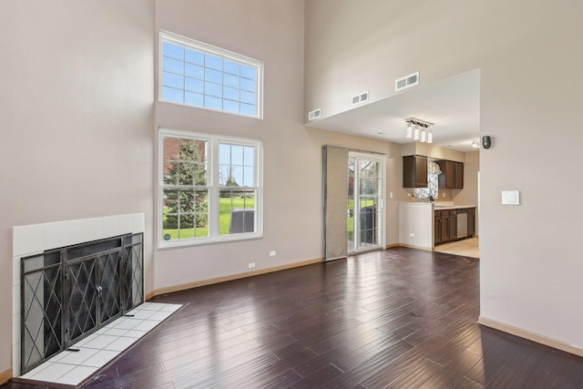 unfurnished living room with baseboards, wood finished floors, a tiled fireplace, plenty of natural light, and a high ceiling