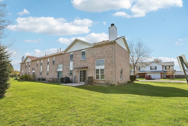 back of house with a yard, a chimney, brick siding, and a patio
