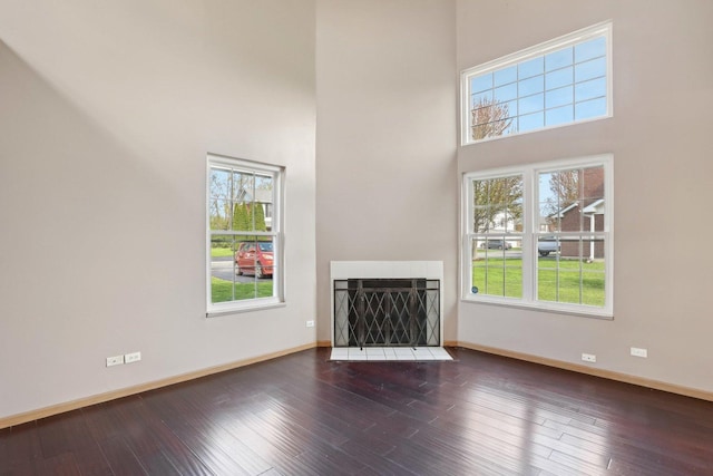 unfurnished living room with wood finished floors, a towering ceiling, and baseboards
