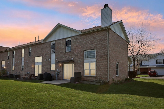 back of house at dusk with a lawn, a chimney, and brick siding