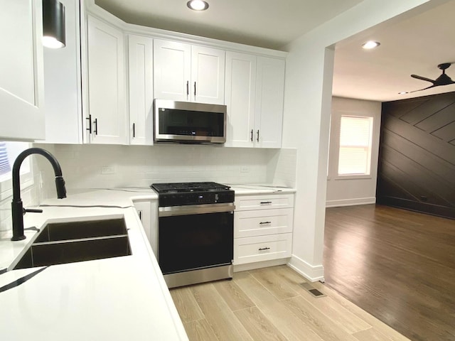 kitchen with stainless steel microwave, white cabinetry, range with gas cooktop, backsplash, and light wood-type flooring