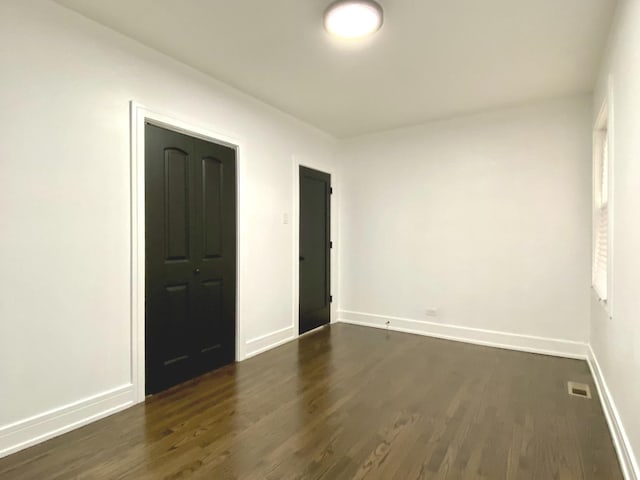 empty room with baseboards, visible vents, and dark wood-type flooring