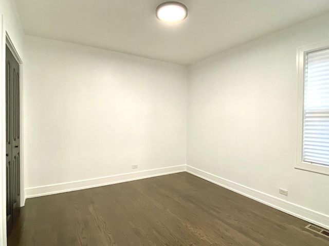 unfurnished room with visible vents, dark wood-style flooring, and baseboards