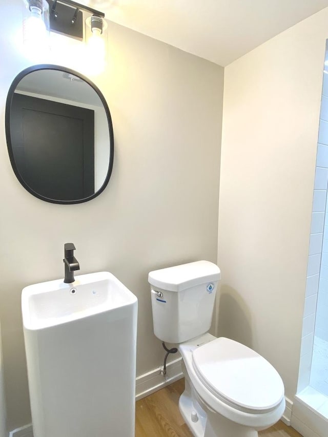 full bathroom featuring toilet, baseboards, tiled shower, and wood finished floors