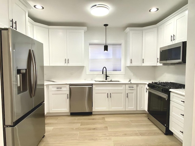 kitchen featuring a sink, stainless steel appliances, decorative light fixtures, white cabinetry, and light countertops