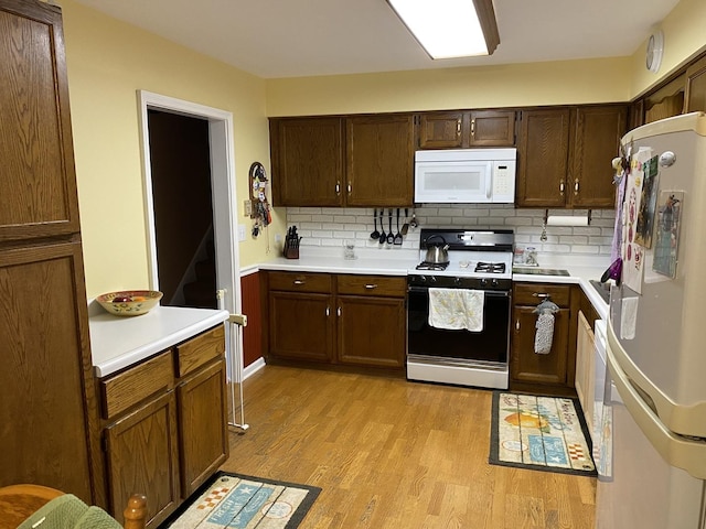 kitchen featuring light wood finished floors, backsplash, light countertops, and white appliances